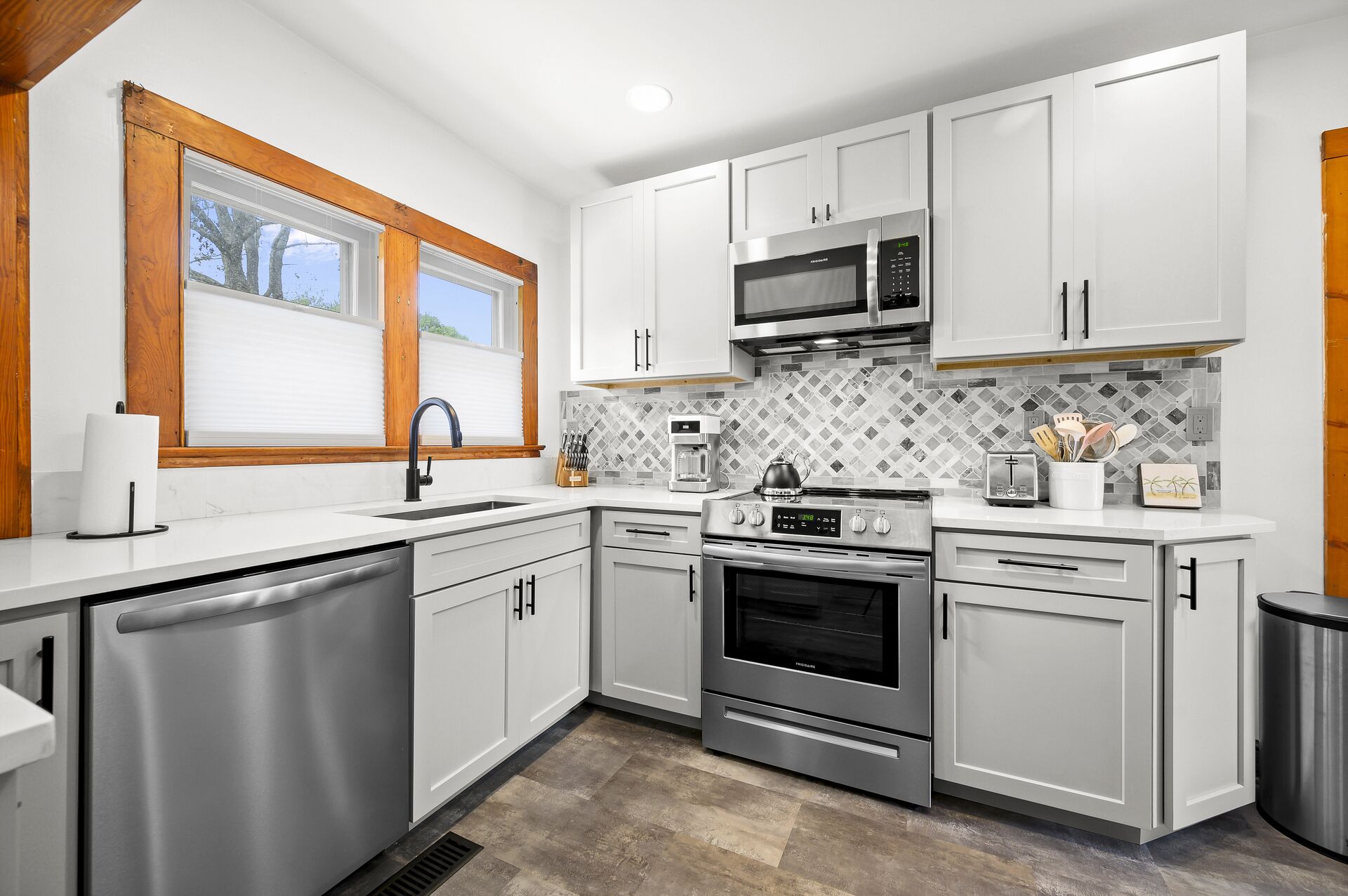 Una cocina moderna con armarios blancos, electrodomésticos de acero inoxidable, una ventana con persianas y un salpicadero de azulejos.