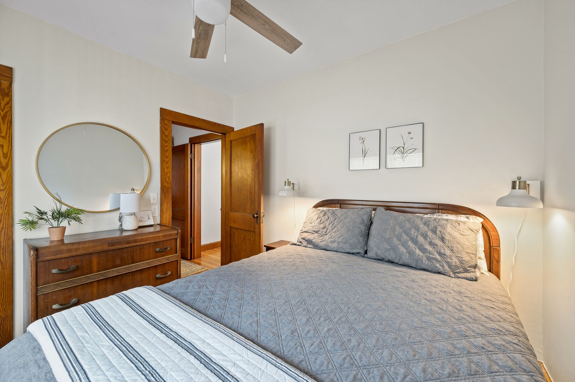 Une chambre à coucher comprenant un lit, une commode, un miroir et deux lampes fixées au mur.