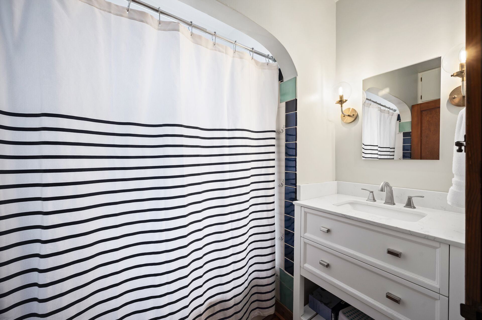 Une salle de bain avec un rideau de douche à rayures, un lavabo blanc, un miroir et un porte-serviettes.
