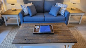 A living room with a blue sofa, two matching nightstands, a wooden coffee table, and a framed picture above the sofa. - SEArenity and Seashells (Myrtle Beach)