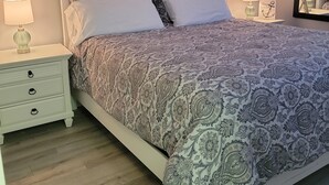 A neatly made bed with patterned bedding, a bedside table with a lamp, and a wall with three framed artworks. - SEArenity and Seashells (Myrtle Beach)