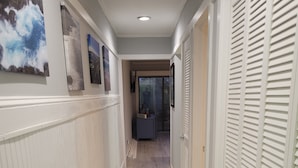A hallway with a wooden floor, white walls, and a door with louvered shutters. - SEArenity and Seashells (Myrtle Beach)