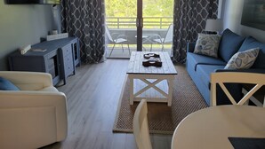 A modern living room with a sofa, a coffee table, a TV, and a balcony with curtains. - SEArenity and Seashells (Myrtle Beach)