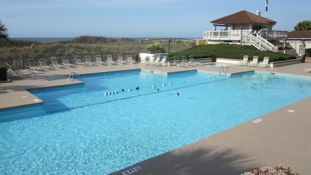 A swimming pool with lounge chairs and a building with a balcony overlooking the beach. - SEArenity and Seashells (Myrtle Beach)