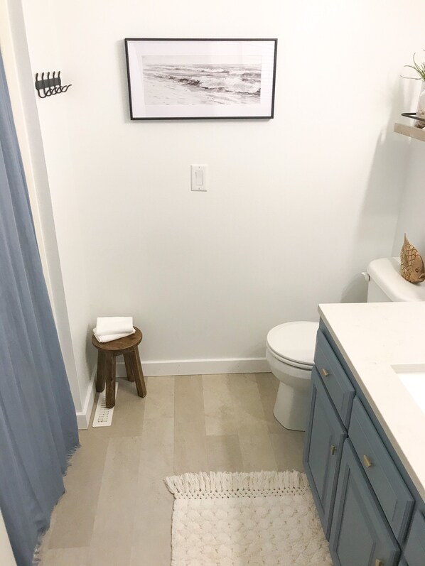 A bathroom with a toilet, a sink, a framed picture on the wall, a small stool, and a blue curtain. - Scenic treetop views at Lake Panorama (Panora)