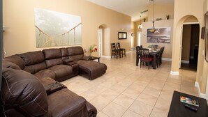 A spacious living room with a large sectional sofa, a dining area with a table and chairs, and a kitchen in the background. - Large 4 Bedroom Villa. 3 Miles to Disney, Private Pool, Games Room (Kissimmee)
