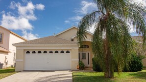 A single-story house with a garage, a small front yard, and a palm tree. - Large 4 Bedroom Villa. 3 Miles to Disney, Private Pool, Games Room (Kissimmee)