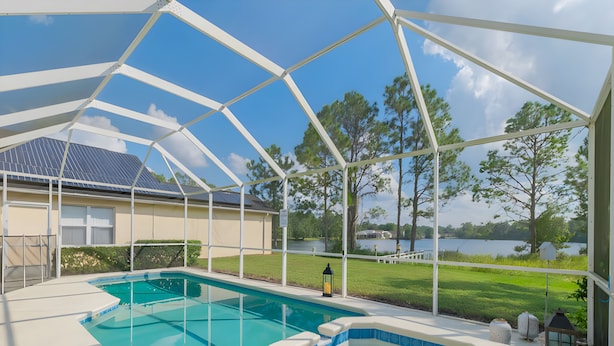 A covered outdoor swimming pool with a hot tub, surrounded by a white pergola, overlooking a lake and trees. - Reserve Relaxing 5 Bedroom Pool Lake View (Davenport)