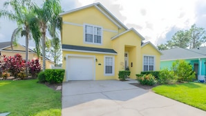 A two-story yellow house with a garage, surrounded by well-maintained lawns and tropical plants. - Reserve Relaxing 5 Bedroom Pool Lake View (Davenport)