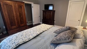 Une chambre à coucher avec un lit, un ventilateur de plafond, un téléviseur posé sur un meuble et une porte.