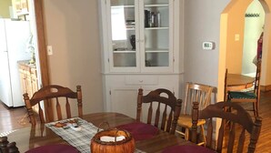 Une salle à manger avec une table en bois, dressée pour quatre personnes, entourée de chaises. Un buffet blanc aux portes vitrées est adossé au mur.