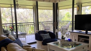 Ein Wohnzimmer mit einer Couch, einem Sessel und einem Couchtisch, einem Fernseher sowie einem Balkon mit Geländer.