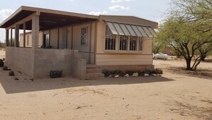 Um pequeno edifício térreo com telhado plano e varanda coberta. Apresenta um design simples e funcional, com fachada de concreto e grades de metal nas janelas.
