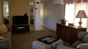 Uma sala de estar com televisão de tela plana em um suporte, sofá, mesa de centro com bandeja, luminária e um armário.