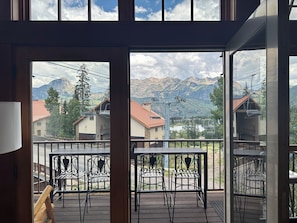Un balcón con sillas y mesas de metal, con vistas a un paisaje montañoso que incluye casas y un telesilla.
