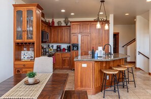 A kitchen with wooden cabinets, a central island with stools, and a dining table with a placemat.