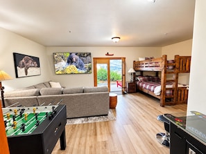 Una sala de estar con sofá, mesa de fútbol, litera y televisor mostrando un oso.