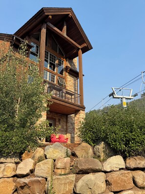 A two-story building with a stone facade, a balcony, and a ski lift in the background.