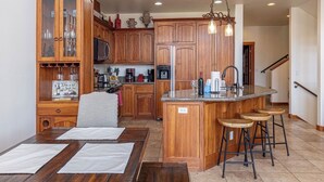 A kitchen with wooden cabinets, a central island with stools, a microwave, and a coffee maker. - ELKPOINT Ski-In/Out .. 4BR/4.5BA .. Sleeps 14 ..  Arcade-Shuffle Board-Foosball (Durango)