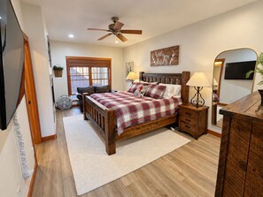A bedroom with a wooden bed, two bedside tables, a ceiling fan, a large window, and a mirror.