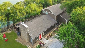A two-story house with a stone foundation, a red door, and a deck overlooking a body of water. - Lakefront, Private Dock, Spectacular Views, Spacious, Modern , 2 Large Decks, Firepit, Gameroom! (Bridgeport)