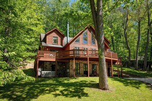 A two-story log cabin with a stone foundation, a balcony, and a stone chimney.