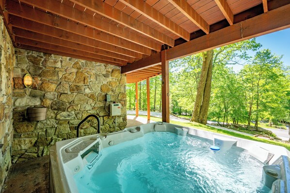 A hot tub under a wooden pergola with stone walls, surrounded by a lush green landscape.