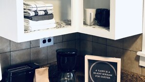 Uma cozinha com estação de café, incluindo cafeteira, um pacote de café e uma placa com a inscrição 'A YAWN IS A SILENT SCREAM FOR COFFEE'.