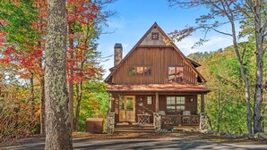A rustic cabin with a stone chimney, wooden exterior, and a porch with outdoor seating. - Bag End at Eagles Nest - Game room, great location in the Villages of Eagles Nest + many amenities (Banner Elk)