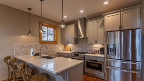 A modern kitchen with stainless steel appliances, a central island with bar stools, and pendant lighting. - Bag End at Eagles Nest - Game room, great location in the Villages of Eagles Nest + many amenities (Banner Elk)