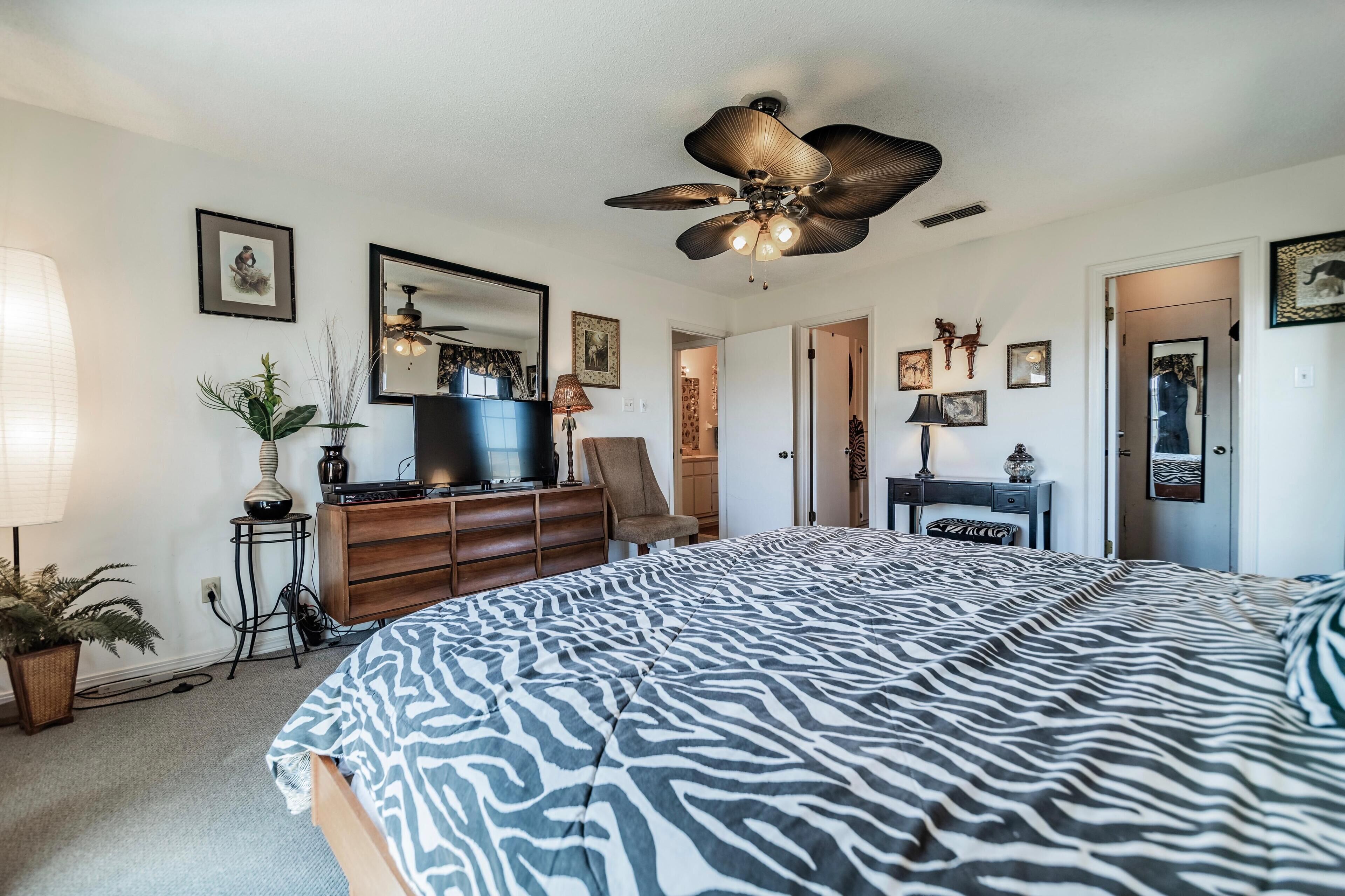 A bedroom with a bed, ceiling fan, dresser, TV, and various wall decorations.