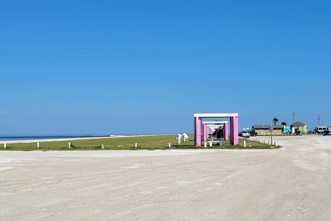 A beachside road with a small pink structure, a clear sky, and a distant view of the ocean.