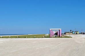 A beachside road with a small pink structure, a clear sky, and a distant view of the ocean.