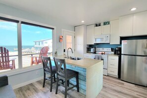 Une cuisine moderne dotée d’un grand îlot central, de meubles blancs et offrant une vue sur la plage par les fenêtres.