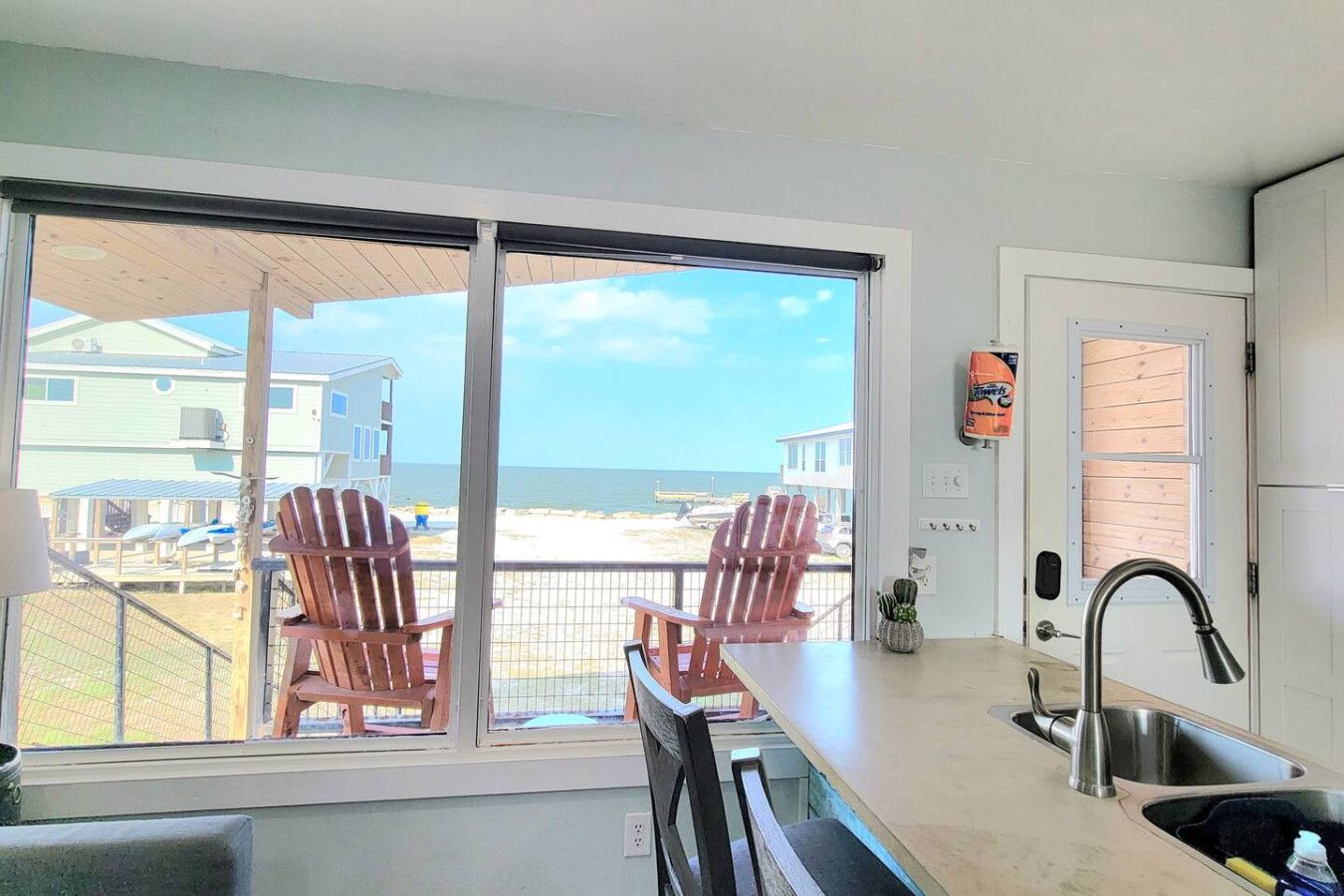 A kitchen with a large window, two wooden chairs, a sink, and a view of the beach.
