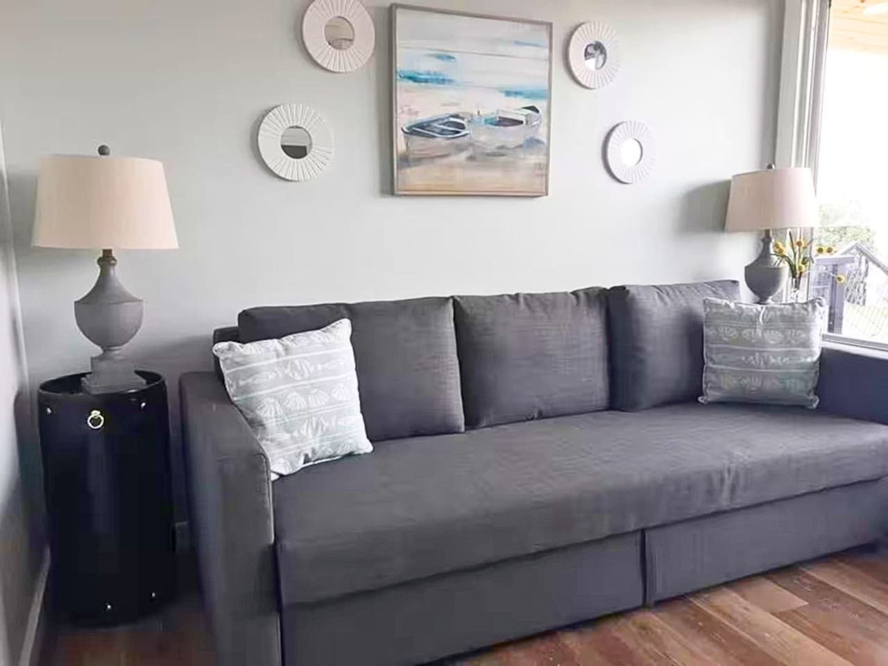 A grey sofa with patterned cushions, a round side table, and a painting on the wall.