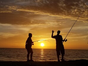 Siluette di due persone che pescano al tramonto, con il sole basso sull'orizzonte.