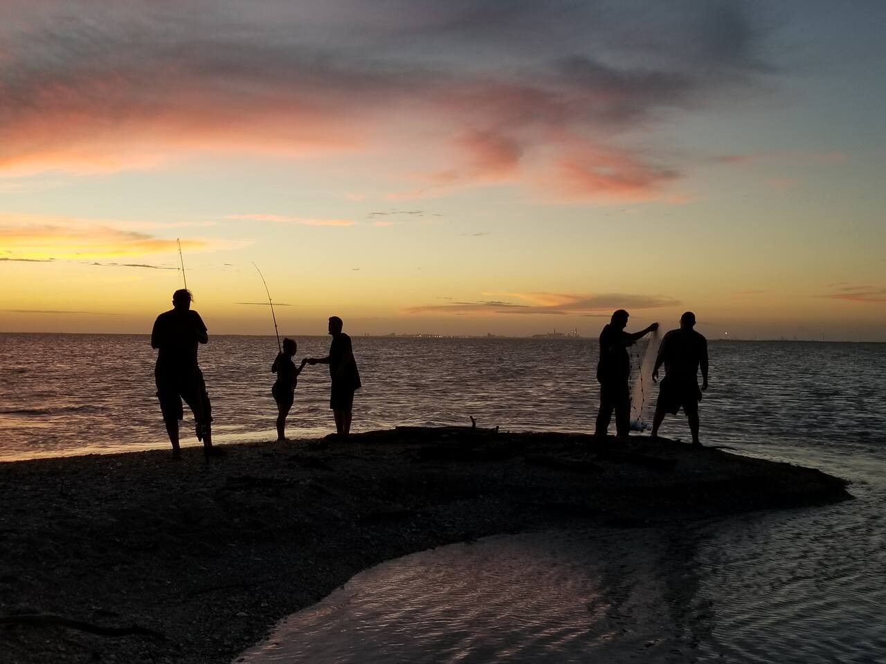 A group of people fishing at sunset on a beach.
