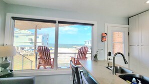 A kitchen with a large sliding glass door leading to a balcony with red chairs, a sink, and a view of the beach. - Casita B · Las Casitas on Magnolia Beach - Casita B (Port Lavaca)