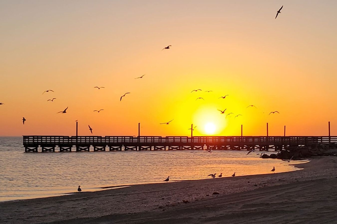 A pier extending into the water with the sun setting in the background.
