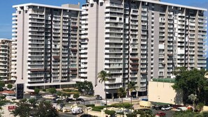 Een hoog appartementencomplex met meerdere balkons, een parkeerplaats en omliggend groen.