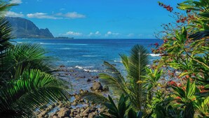 A tropical beach with clear blue water, rocky shore, and lush greenery. - Panoramic Breathtaking Ocean-Sunset-Bali Hai Views A/C + Surf Crashing Below! (Princeville)