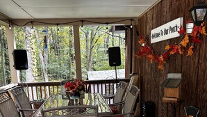 Un patio in legno con sedie in vimini e un tavolo, un cartello con la scritta 'Benvenuti sul nostro portico' e una zucca intagliata.