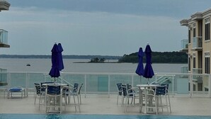 A pool with lounge chairs and umbrellas, overlooking a body of water with a distant shoreline.