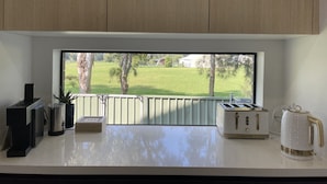 Una cocina con vista a un campo verde y árboles, con una tostadora, un hervidor y una cafetera sobre la encimera.