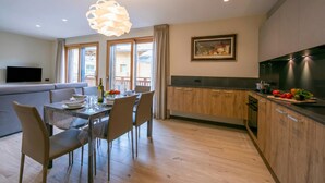 A modern kitchen with wooden cabinets, a dining area with a glass table, and a living area with a sofa. - Casa Luminosa Ski in -Ski out 100m, Livigno, Italy (Livigno)