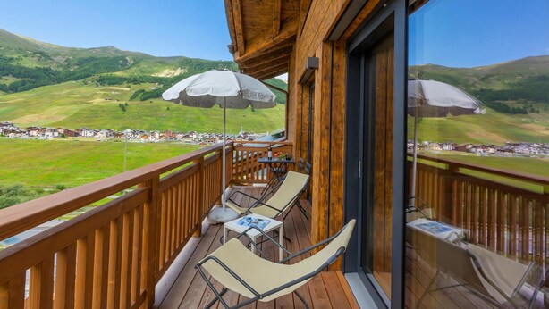 A wooden deck with two lounge chairs and a table, overlooking a green valley with houses. - Casa Luminosa Ski in -Ski out 100m, Livigno, Italy (Livigno)