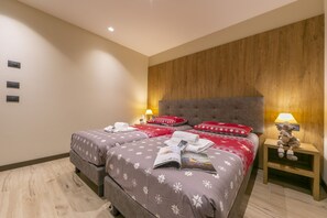 Une chambre d’hôtel avec deux lits, une tête de lit en bois, des lampes de chevet et une petite table de chevet sur laquelle est posé un ours en peluche.