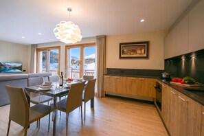 A modern kitchen with wooden cabinets, a dining area with a table set for four, and a large window with a view of mountains. - Casa Luminosa Ski in -Ski out 100m, Livigno, Italy (Livigno)