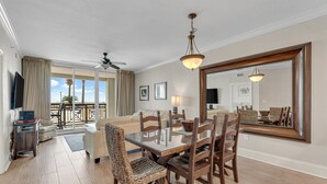 A spacious living room with a glass dining table, wooden chairs, a ceiling fan, and a large mirror on the wall. - Azure 110 walkout closest unit to beach access, no Elevator Rides! Beach Service (Fort Walton Beach)